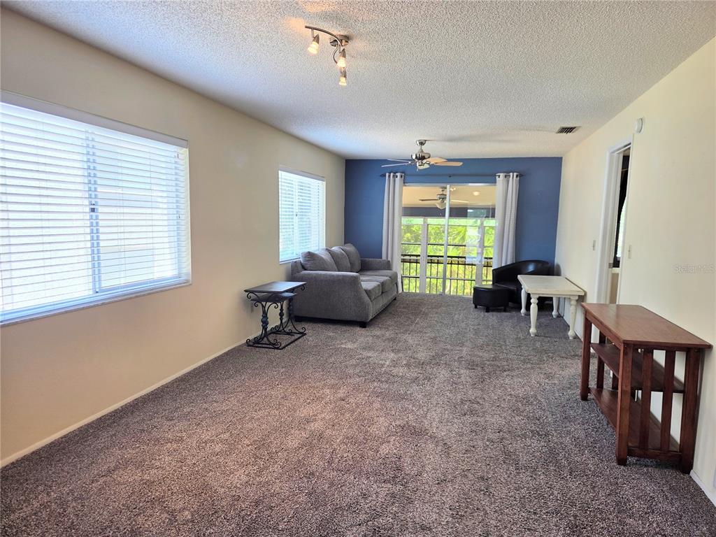 A living room with gray carpet, a blue accent wall, and a sliding glass door — 12404 EAGLESWOOD DRIVE UNIT C, HUDSON, FL