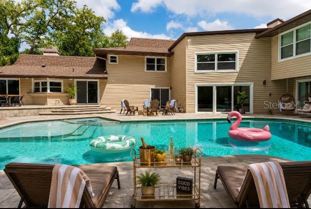 A stone fire pit with Adirondack chairs sits on a patio beside a swimming pool — 1584 OAK LANE, CLEARWATER, FL