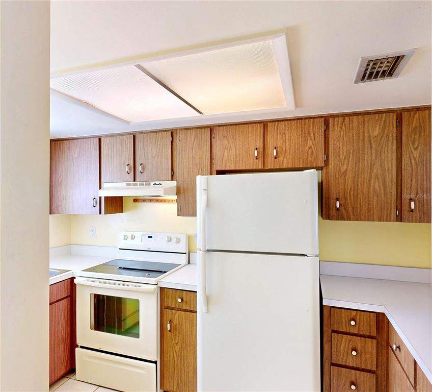 A kitchen features wood cabinets, white appliances, a drop ceiling light, and light-colored countertops — 404 E ORLANDO AVENUE UNIT 8B, OCOEE, FL