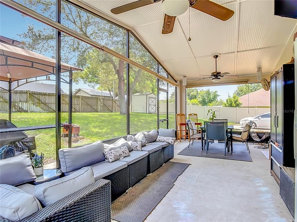 A grassy backyard features a large oak tree, a screened-in patio, and a vinyl privacy fence — 1123 W HANCOCK DRIVE, DELTONA, FL