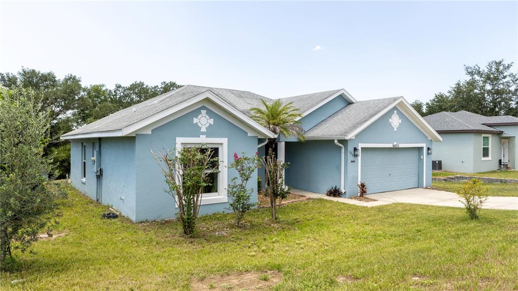 A blue single-story house with a two-car garage and a front yard with small trees — 16023 WORTHINGTON, MASCOTTE, FL