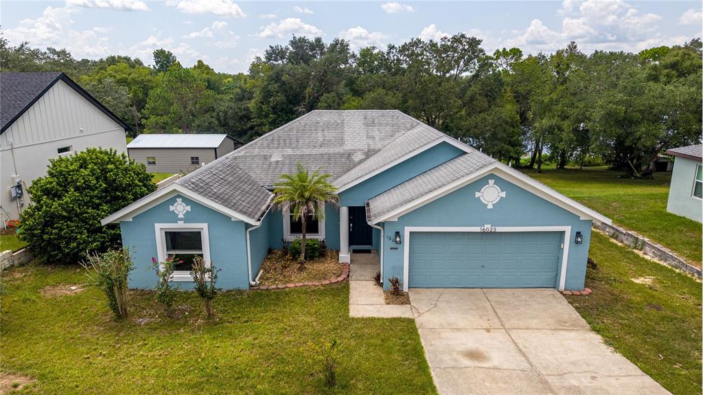 A blue single-story house with a two-car garage and a gray shingled roof — 16023 WORTHINGTON, MASCOTTE, FL