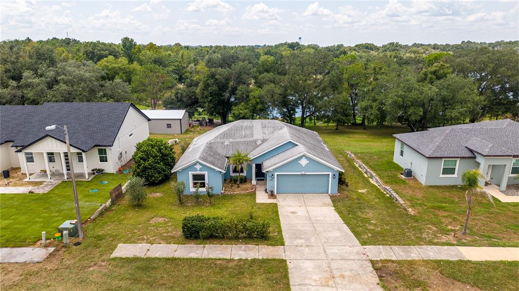 An aerial view shows a blue single-story house with a concrete driveway and surrounding lawn — 16023 WORTHINGTON, MASCOTTE, FL