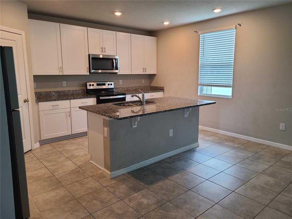 A kitchen features white cabinets, granite countertops, a center island, and gray tile flooring — 10217 DAYBREAK GLEN, PARRISH, FL
