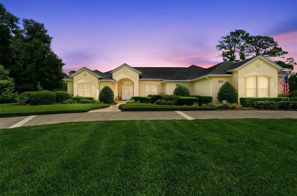 A single-story yellow house with a dark roof and a curved driveway at dusk — 1681 TIMBER EDGE DRIVE, DELAND, FL
