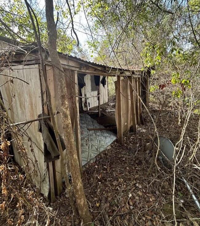 A dilapidated, partially collapsed wooden structure sits in a wooded area with a mattress inside — 0 SE 141ST PLACE, UMATILLA, FL