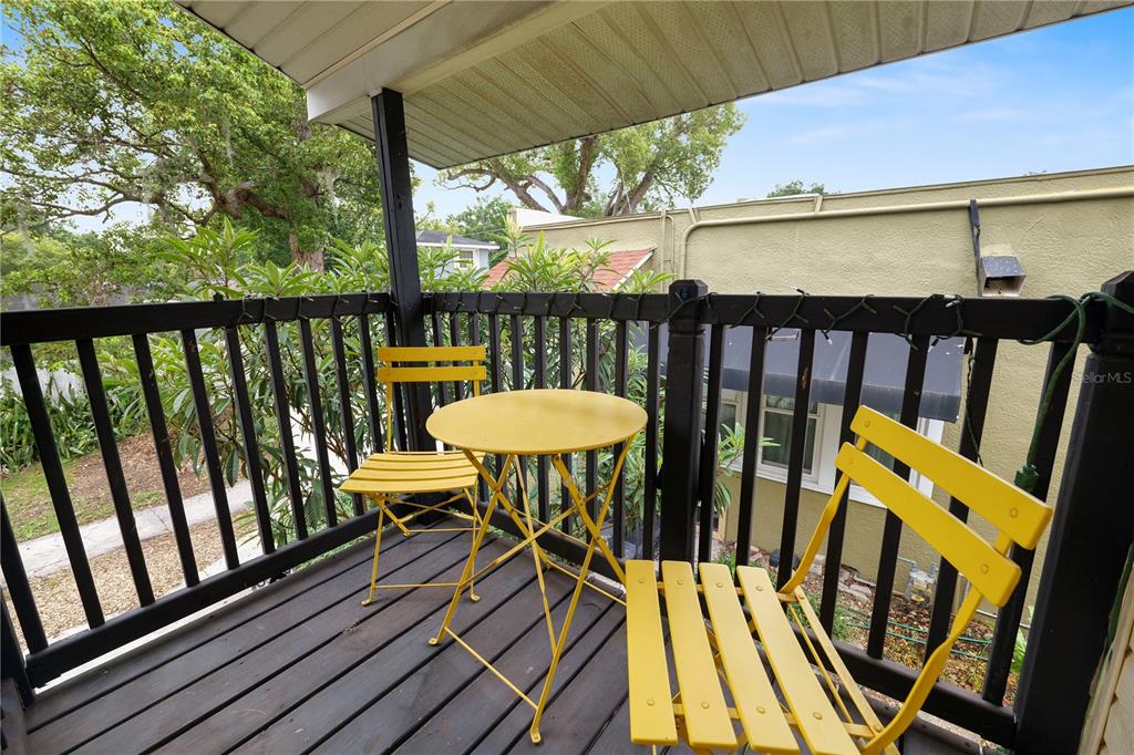 A small wooden balcony features a yellow bistro set against a black railing — 1157 E EDGEWOOD DRIVE UNIT C, LAKELAND, FL