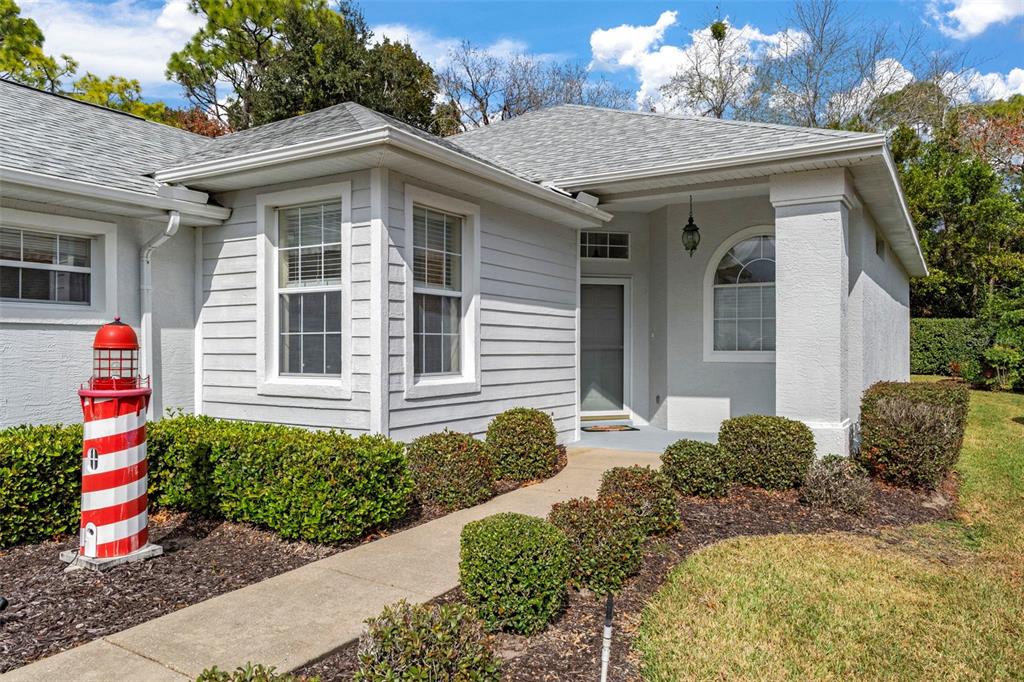 A light-colored house exterior features a front walkway, manicured bushes, and a decorative lighthouse statue — 15 W BYRSONIMA LOOP, HOMOSASSA, FL