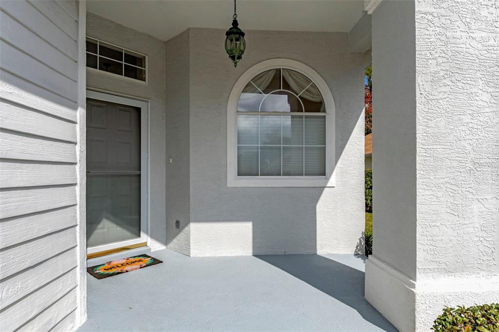 A covered front porch features a light gray floor, a white door, and an arched window — 15 W BYRSONIMA LOOP, HOMOSASSA, FL