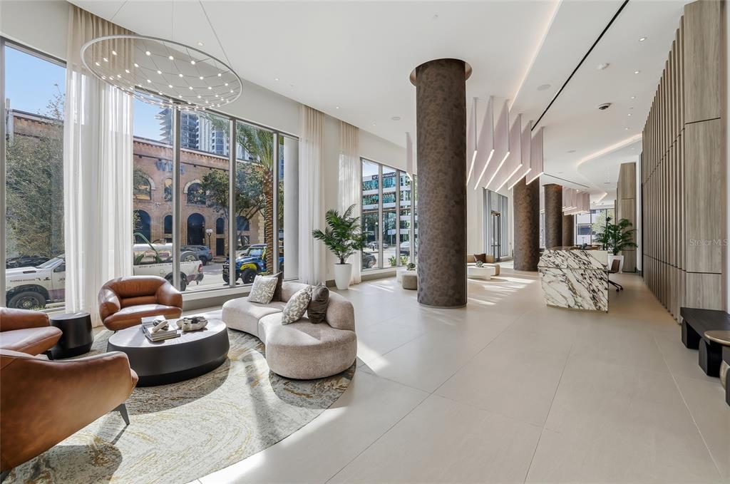 A modern lobby features floor-to-ceiling windows, circular columns, a marble reception desk, and lounge seating — 275 1ST AVENUE S UNIT 1003, ST PETERSBURG, FL