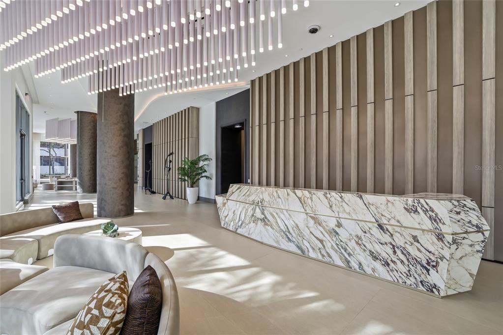 A modern lobby features a marble reception desk, vertical wood wall panels, and pendant lighting — 275 1ST AVENUE S UNIT 1003, ST PETERSBURG, FL