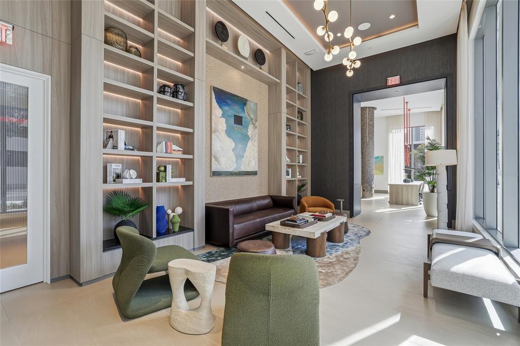 A modern lounge area features a leather sofa, green armchairs, built-in shelving, and a chandelier — 275 1ST AVENUE S UNIT 1003, ST PETERSBURG, FL