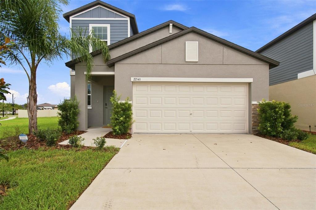 A two-story suburban house features a beige stucco facade, a two-car garage, and blue siding — 22141 STORYBOOK CABIN WAY, LAND O LAKES, FL