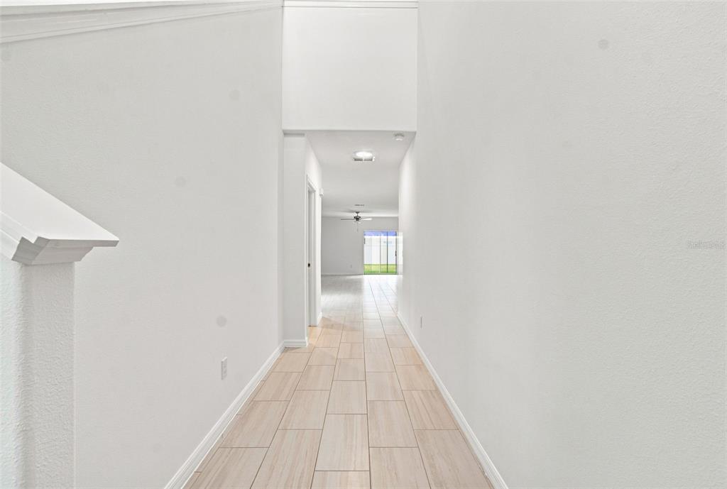 A long, narrow hallway with light-colored tile flooring leads toward an open living area — 22141 STORYBOOK CABIN WAY, LAND O LAKES, FL