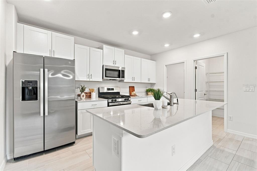 A modern kitchen features white cabinets, stainless steel appliances, and a central quartz-topped island — 22141 STORYBOOK CABIN WAY, LAND O LAKES, FL