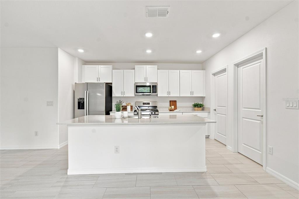 A modern kitchen features white cabinetry, stainless steel appliances, and a large central island — 22141 STORYBOOK CABIN WAY, LAND O LAKES, FL