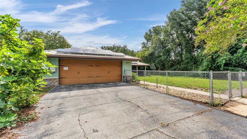 A house exterior features a brown garage door, solar panels, and a chain-link fenced yard — 1002 W LAKE MARION ROAD, HAINES CITY, FL