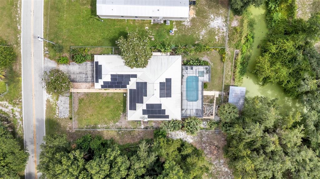 An aerial view shows a house with solar panels, a screened pool, and surrounding trees — 1002 W LAKE MARION ROAD, HAINES CITY, FL