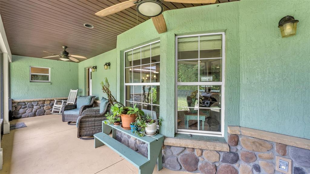 A covered patio features green stucco walls, stone wainscoting, ceiling fans, and outdoor wicker furniture — 1002 W LAKE MARION ROAD, HAINES CITY, FL