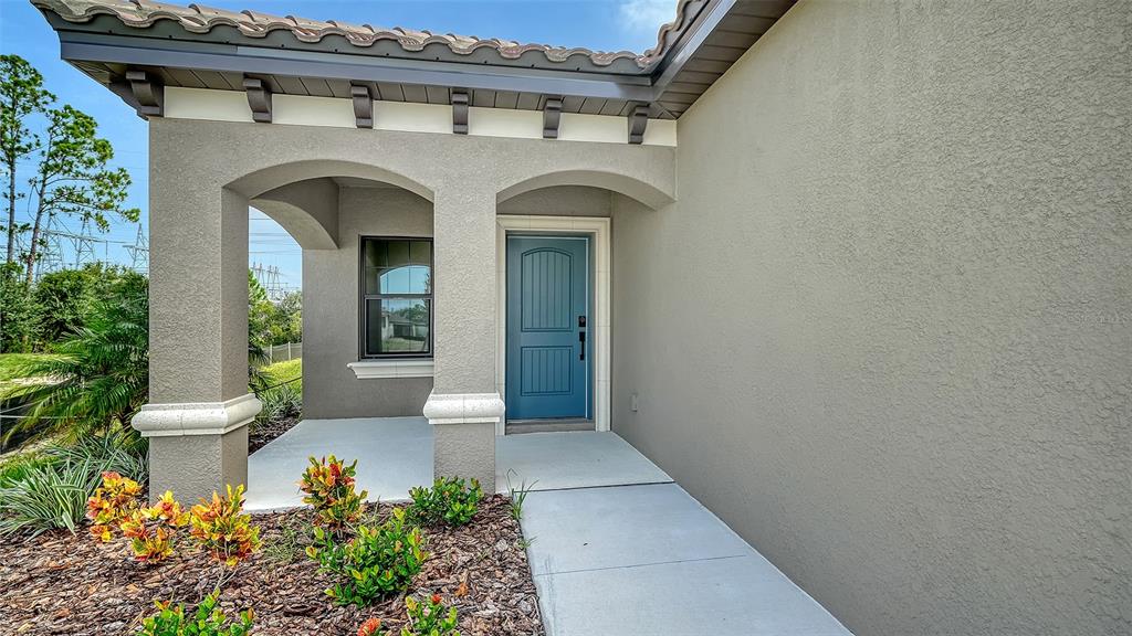 A covered entryway features a blue front door, stucco walls, and a tiled roof — 345 POTENZA LOOP, NOKOMIS, FL