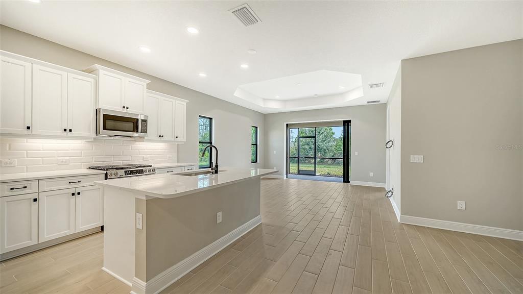 A modern kitchen with white cabinets and an island opens to a living area outdoors — 345 POTENZA LOOP, NOKOMIS, FL