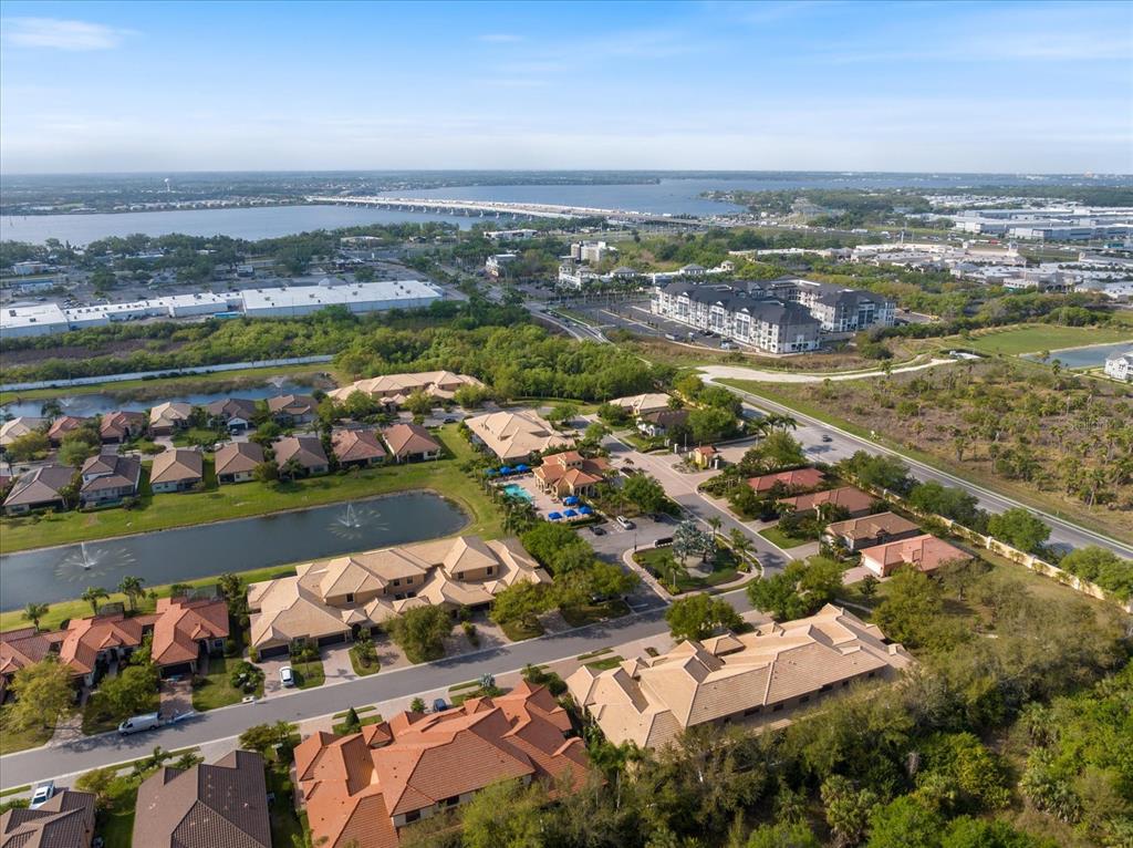 An aerial view shows a suburban neighborhood with houses, a pond, and a nearby bridge — 6120 E 27 STREET E, ELLENTON, FL