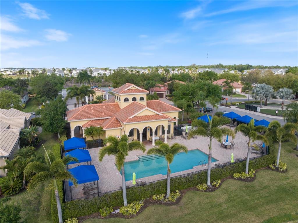 An aerial view shows a community clubhouse with a swimming pool and blue shade structures — 6120 E 27 STREET E, ELLENTON, FL