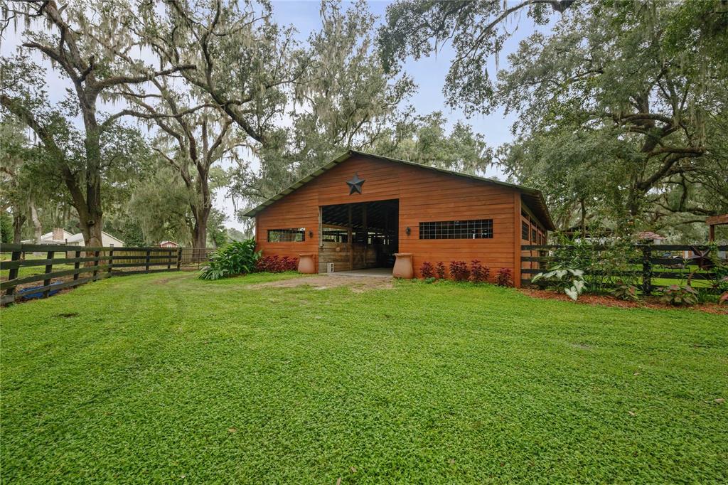 A wooden barn with a metal roof stands in a grassy yard under large trees — 4457 CR 542H, BUSHNELL, FL