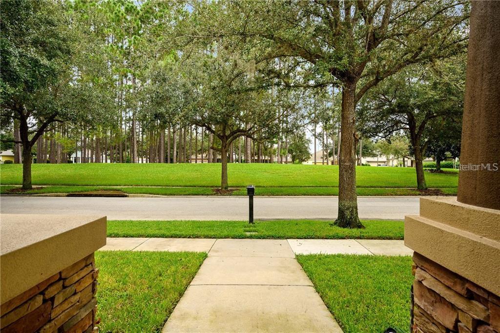 A view from a front porch looking across a sidewalk toward a grassy lot and trees — 6971 NOBLETON DRIVE, WINDERMERE, FL