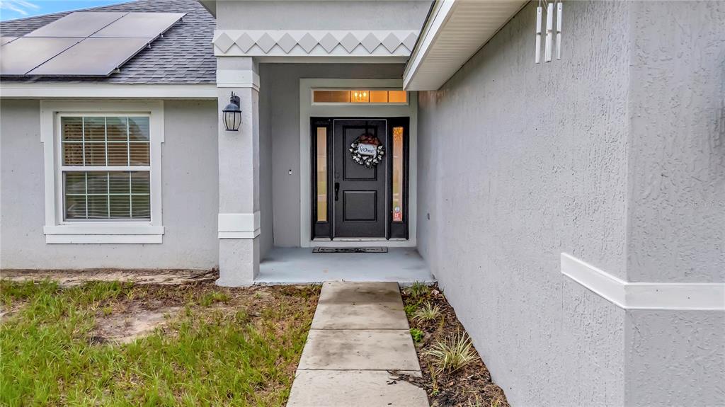 A concrete walkway leads to the front entrance of a gray house with solar panels — 8241 SW 132 LOOP, OCALA, FL