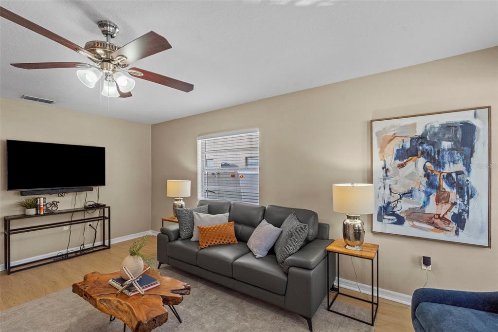 A living room features a grey sofa, a live-edge coffee table, and a wall-mounted television — 7610 S SHERRILL STREET, TAMPA, FL