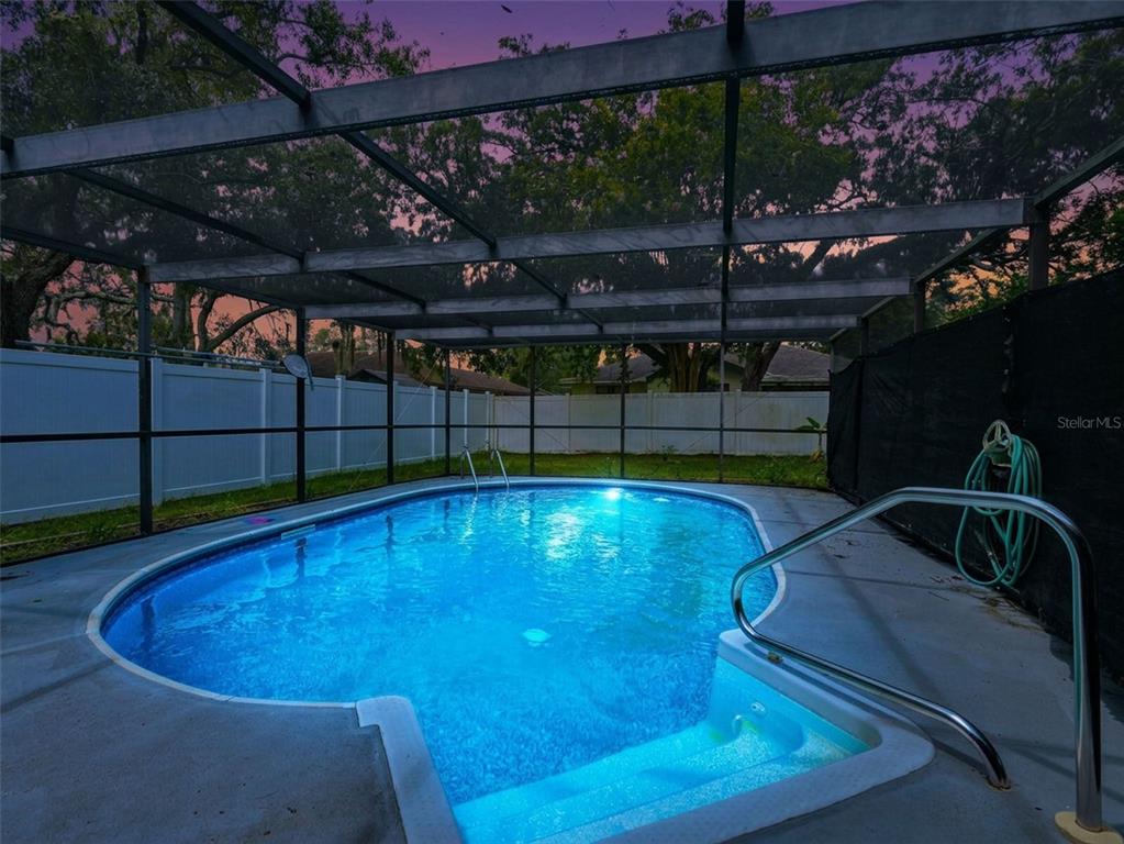 A screened-in backyard swimming pool with a white vinyl fence at dusk — 1139 DESMOND AVENUE, SPRING HILL, FL