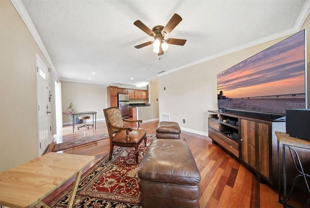 A living room with hardwood floors, a ceiling fan, a large television, and an adjacent kitchen — 4890 CONWAY ROAD UNIT 66, ORLANDO, FL
