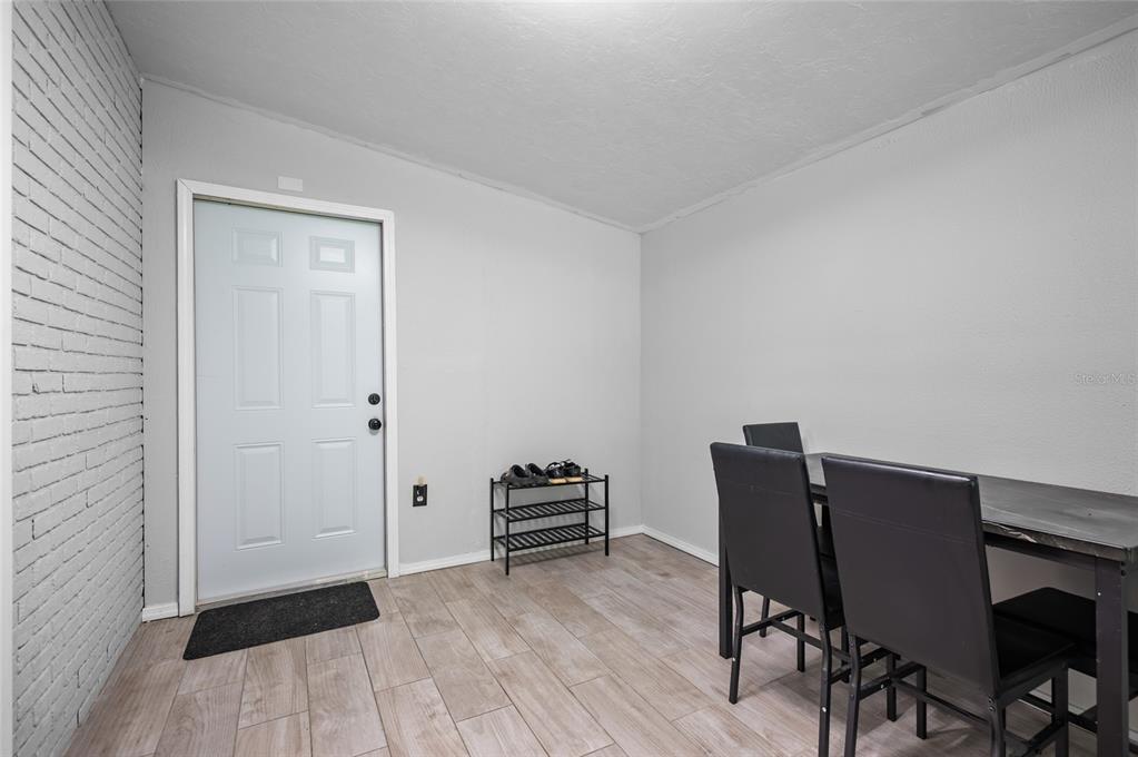 A room with light wood-look tile floors, a white door, and a black dining set — 340 TIMBRUCE LANE NW, PORT CHARLOTTE, FL