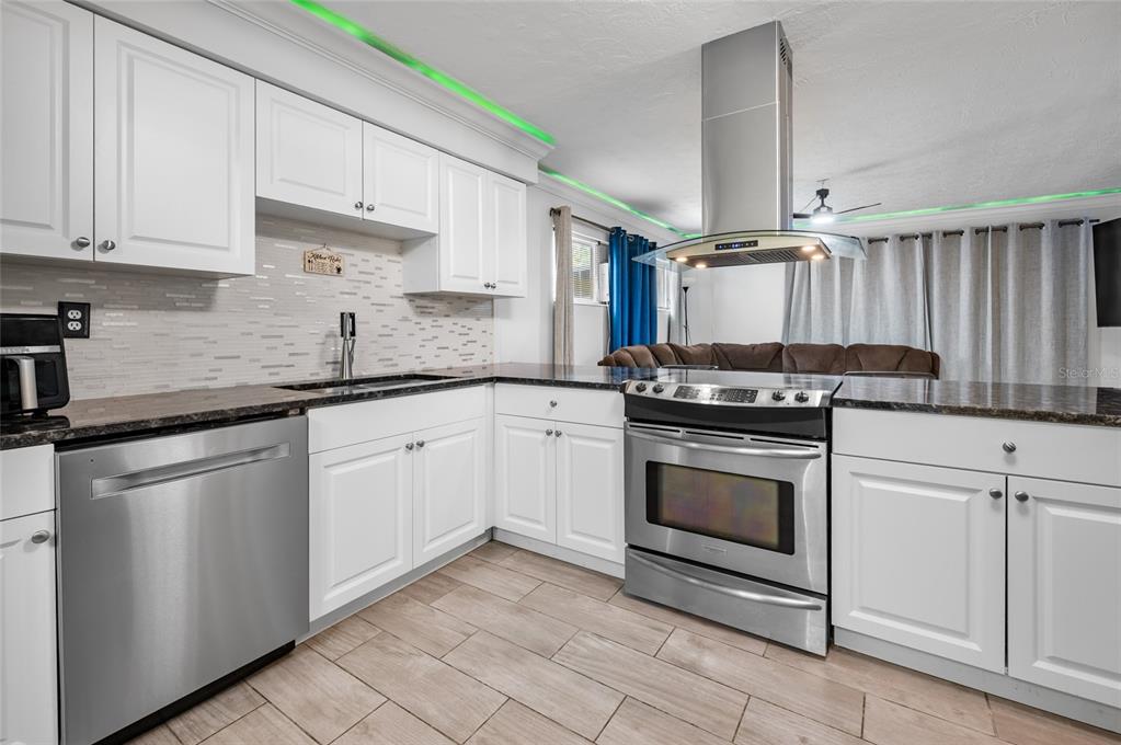 A kitchen features white cabinets, stainless steel appliances, dark countertops, and green LED ceiling lighting — 340 TIMBRUCE LANE NW, PORT CHARLOTTE, FL