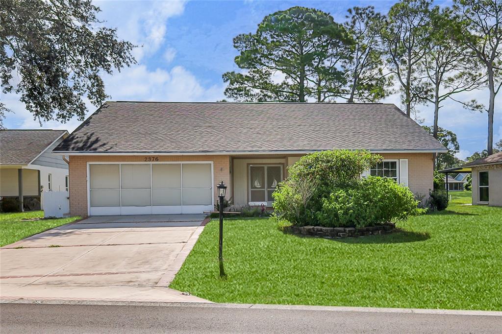 A single-story brick house with a two-car garage, a front lawn, and a large bush — 2376 BENT PINE COURT, SPRING HILL, FL
