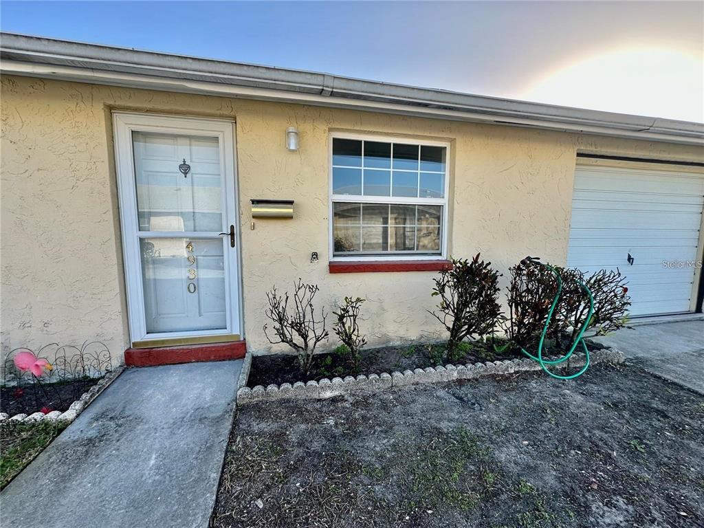 The exterior of a single-story home features a white front door, window, and garage door — 4930 GETNER STREET UNIT 0, NEW PORT RICHEY, FL