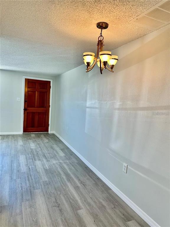 A room with light gray wood-look flooring, a chandelier, and a wooden door — 4930 GETNER STREET UNIT 0, NEW PORT RICHEY, FL