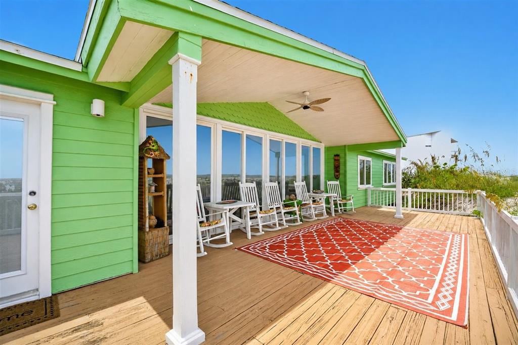 A green house features a wooden deck with a large red patterned rug and chairs — 921 N ATLANTIC AVENUE, NEW SMYRNA BEACH, FL