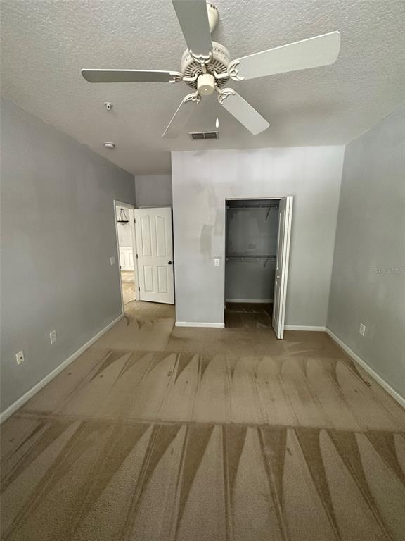 A bedroom with gray walls, beige carpet, a ceiling fan, and an open closet — 6005 NEWPORT LANE UNIT 103, ORLANDO, FL