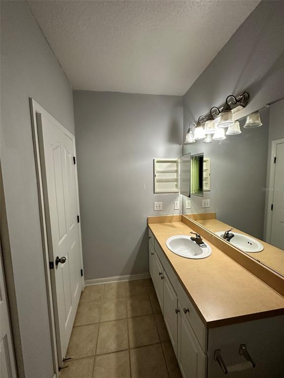 A bathroom features a vanity with a beige countertop, a large mirror, and tiled flooring — 6005 NEWPORT LANE UNIT 103, ORLANDO, FL