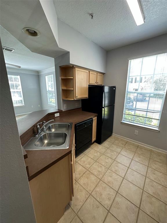A kitchen features light wood cabinets, dark countertops, a black refrigerator, and tile flooring — 6005 NEWPORT LANE UNIT 103, ORLANDO, FL