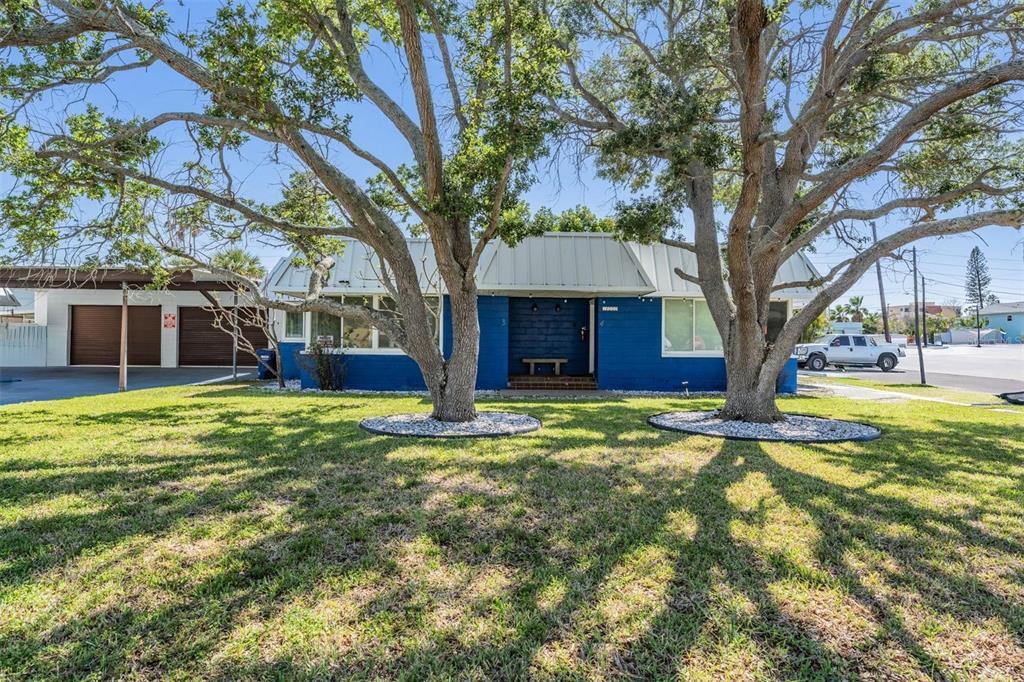 A blue, single-story house with a metal roof and two large trees in the front yard — 14060 MIRAMAR AVENUE, ST PETERSBURG, FL