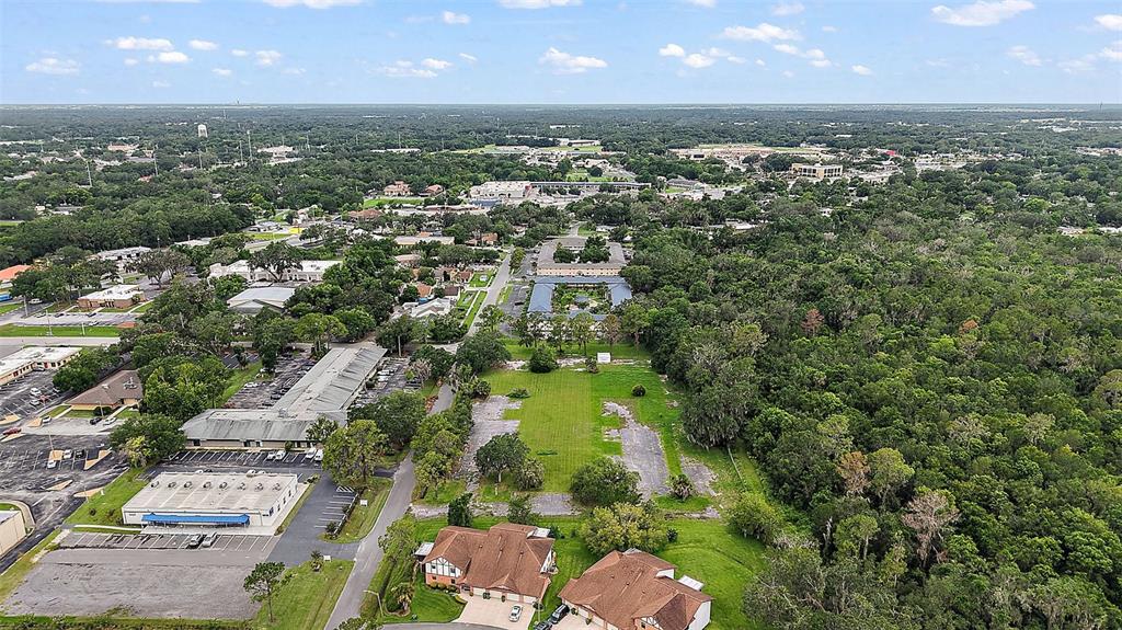 An aerial view shows a vacant lot surrounded by commercial buildings, residential homes, and trees — W OAK TERRACE DRIVE, LEESBURG, FL