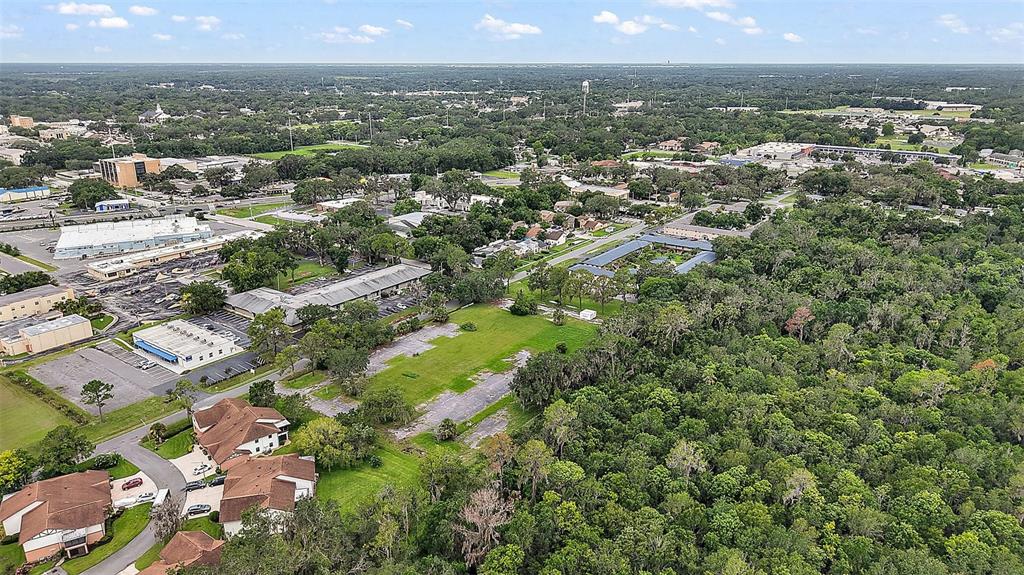 An aerial view shows a large, partially paved vacant lot surrounded by trees and buildings — W OAK TERRACE DRIVE, LEESBURG, FL