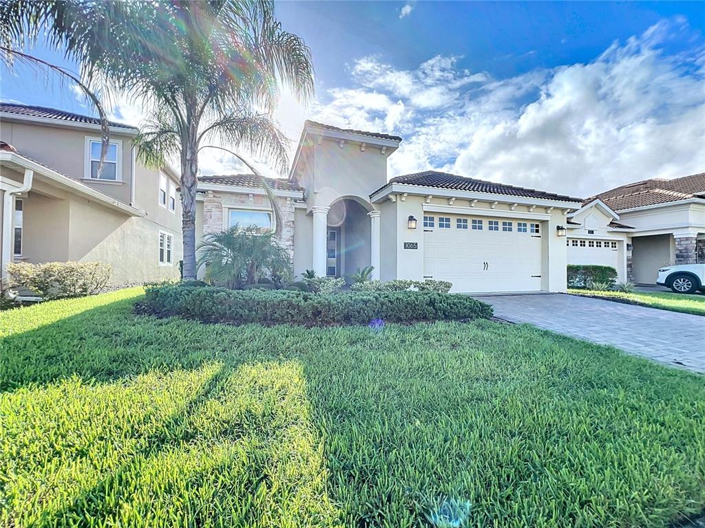 A single-story suburban house with a two-car garage, stone accents, and a palm tree — 1065 BLACKWOLF RUN RD, DAVENPORT, FL