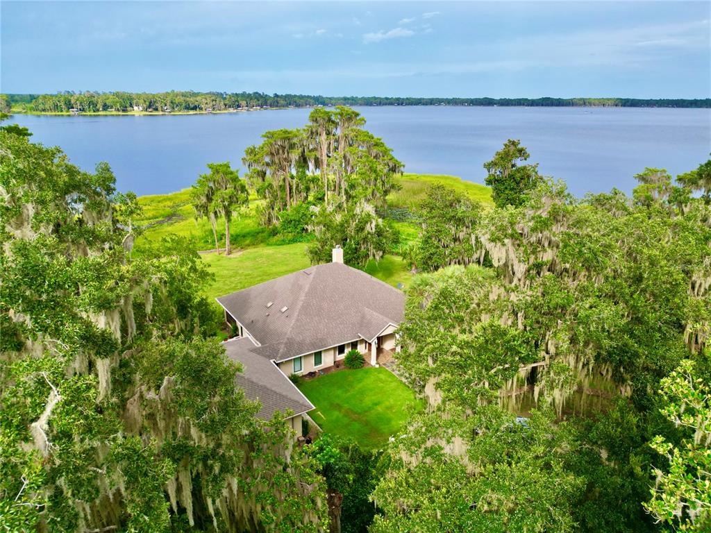An aerial view of a house with a brown roof surrounded by trees near a lake — 20924 NE 132ND AVENUE, WALDO, FL