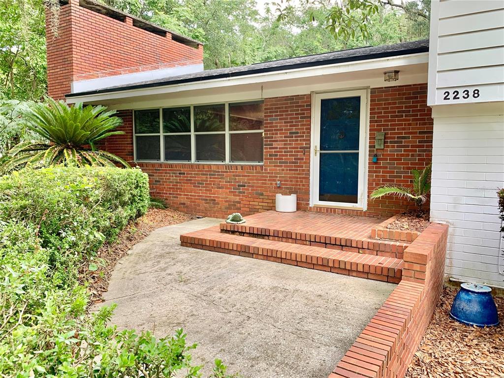 A brick house exterior features a concrete patio, steps to the front door, and landscaping — 2238 NW 16TH AVENUE, GAINESVILLE, FL