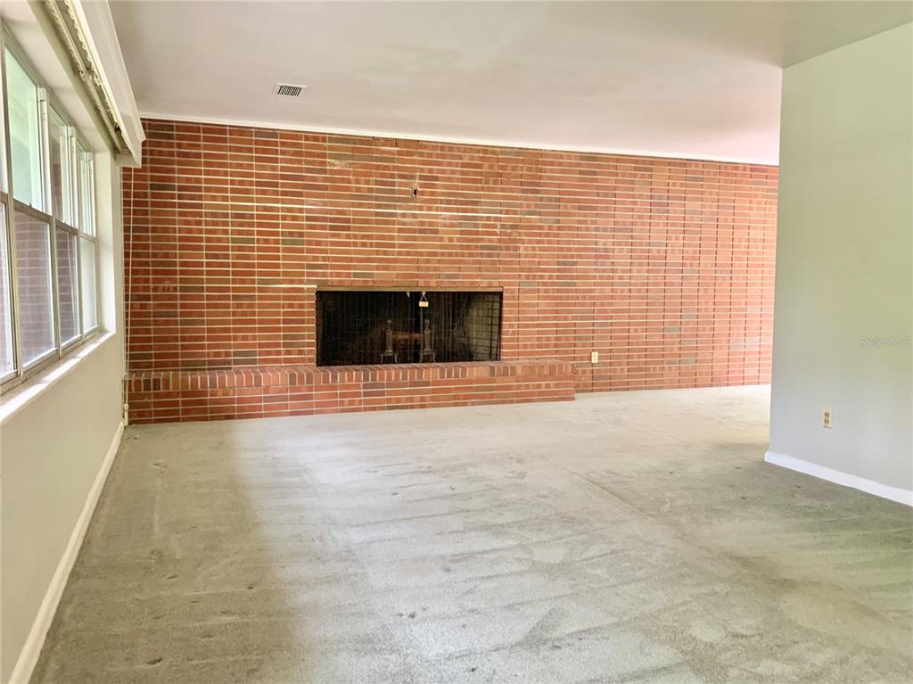 A living room features a large brick fireplace wall, gray carpeting, and windows on the left — 2238 NW 16TH AVENUE, GAINESVILLE, FL
