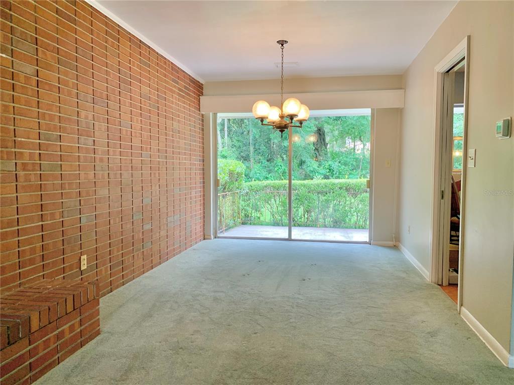 A dining room features a brick accent wall, green carpeting, and sliding glass doors to outside — 2238 NW 16TH AVENUE, GAINESVILLE, FL